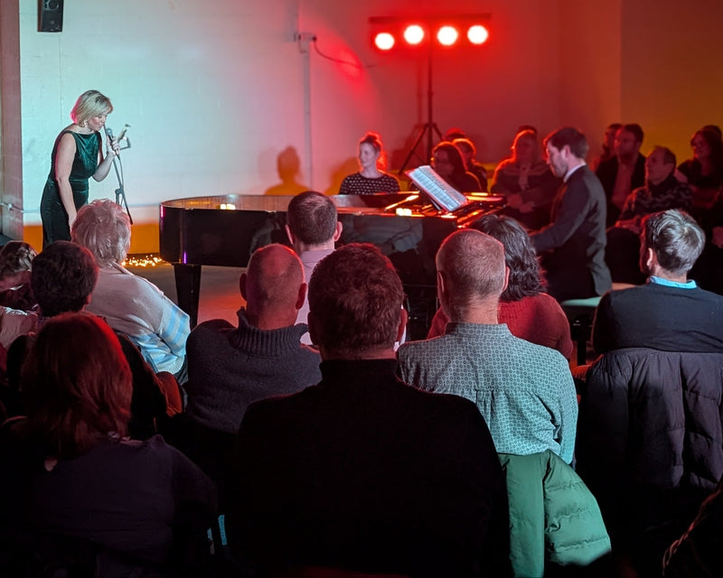 Person on stage speaking to an audience in a room with pink lighting.